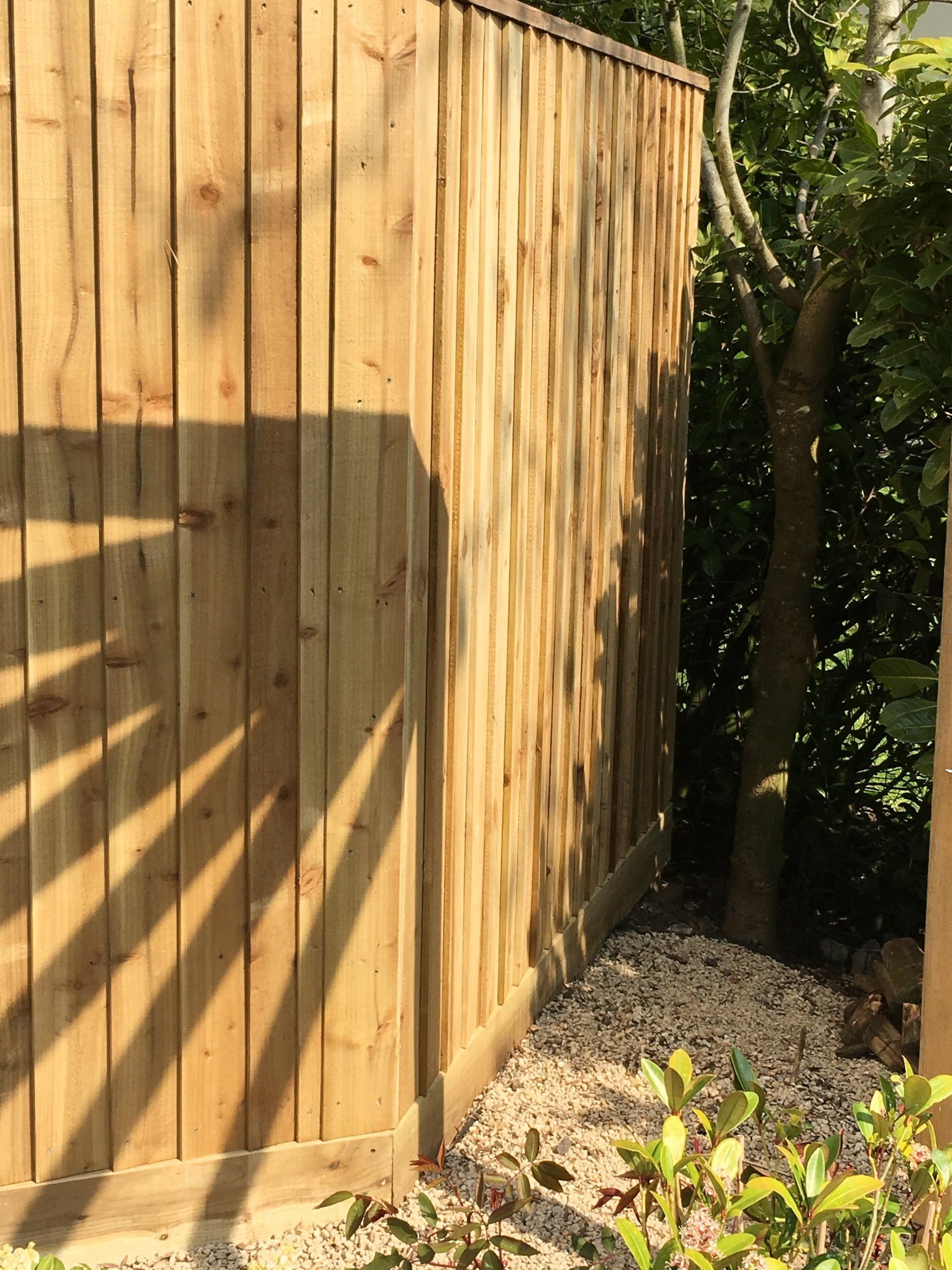 A wooden fence is surrounded by gravel and trees.