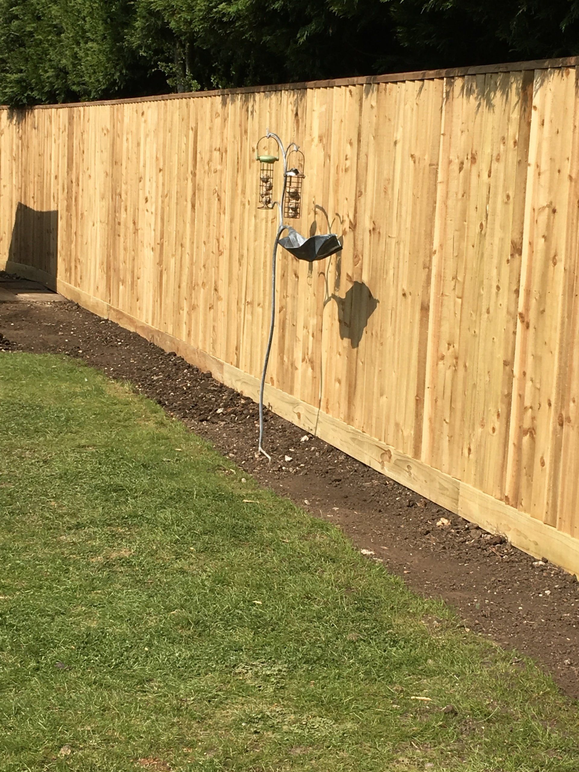 A wooden fence with a bird feeder attached to it in a backyard.