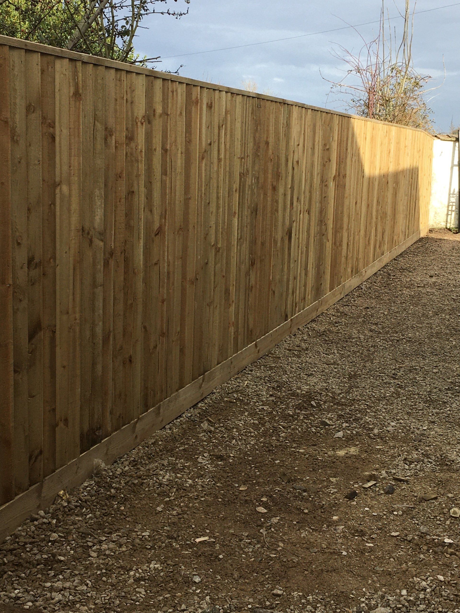 A wooden fence surrounds a gravel area in a backyard.