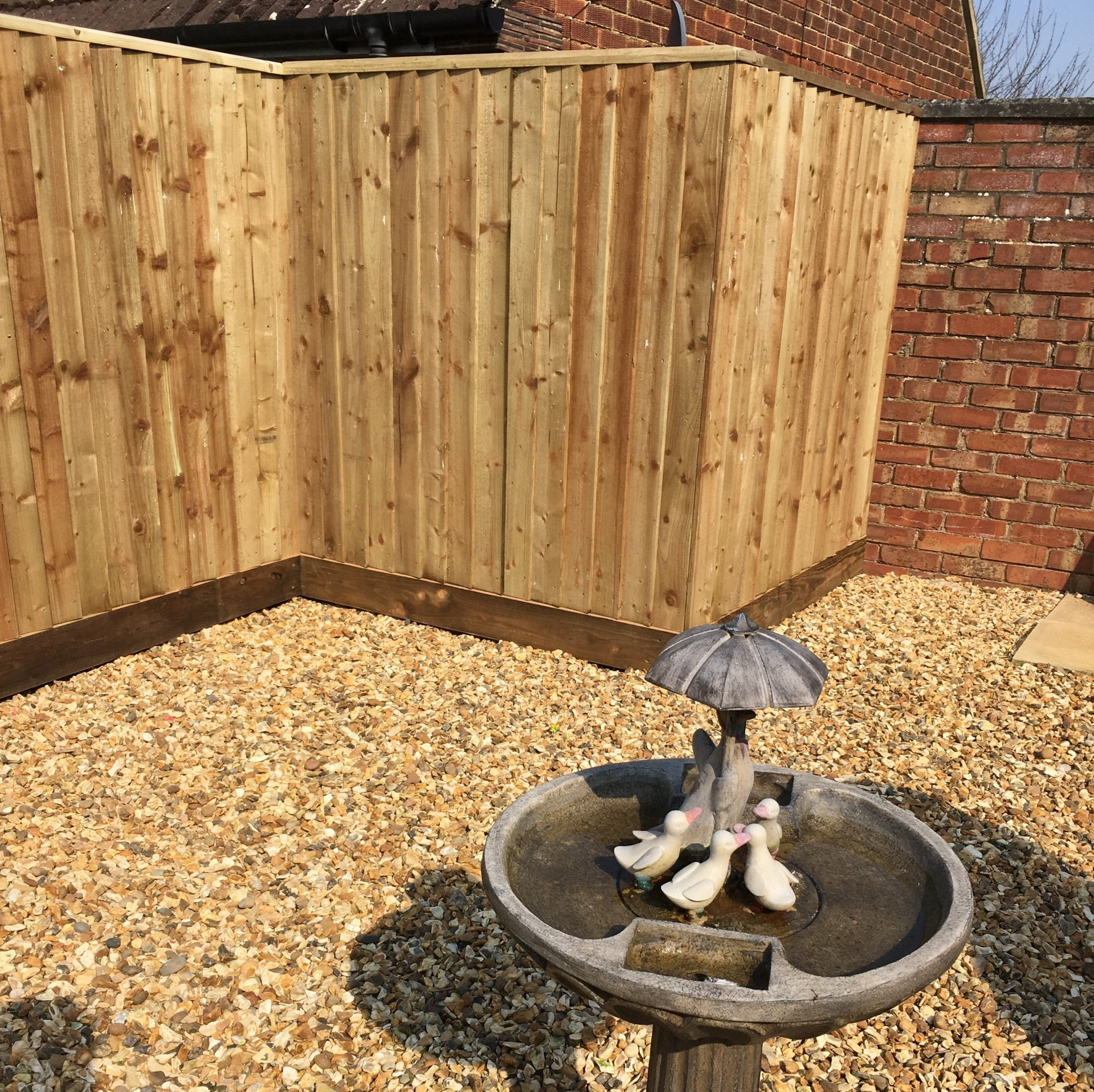 A fountain with ducks and an umbrella in front of a wooden fence