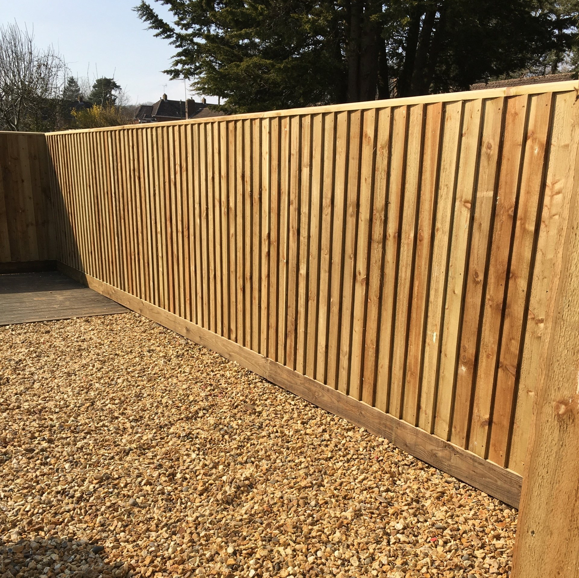 A wooden fence surrounds a gravel area with trees in the background