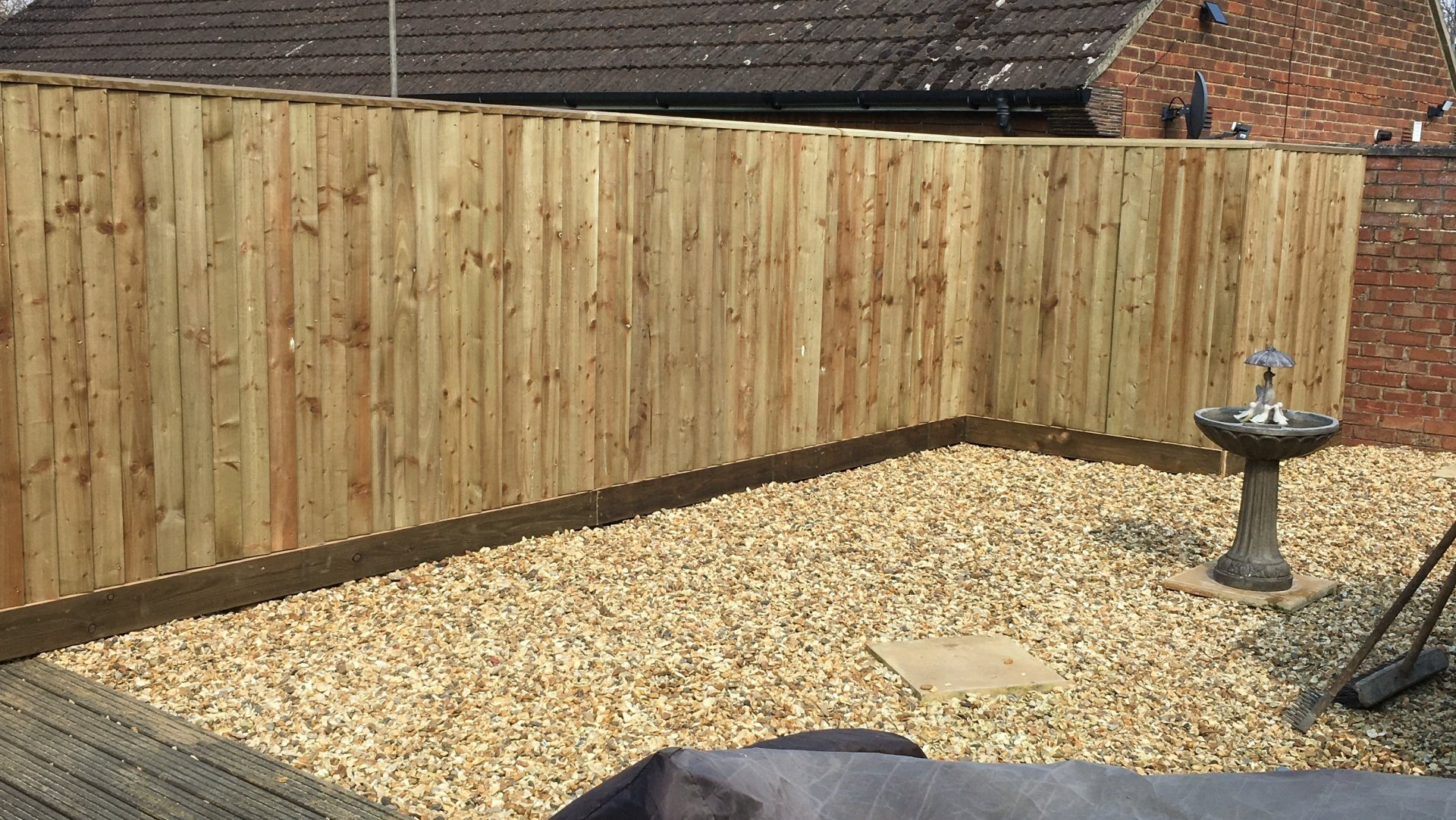 A wooden fence surrounds a gravel area in a backyard.