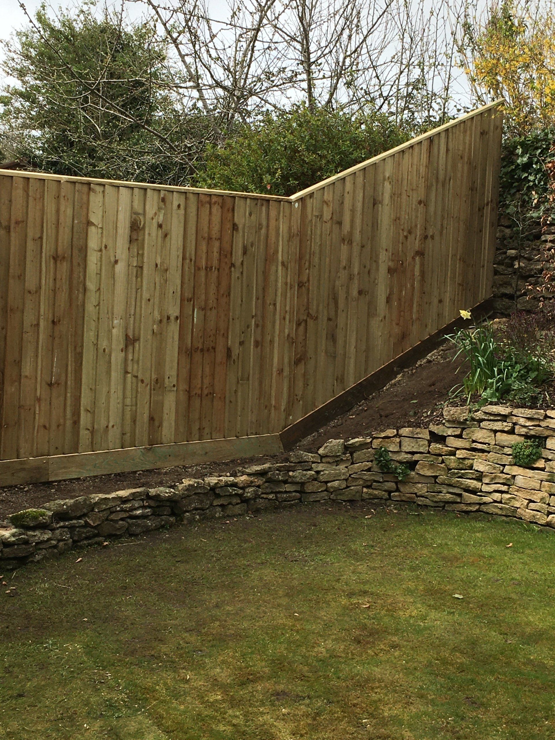 A wooden fence is surrounded by a stone wall in a backyard.