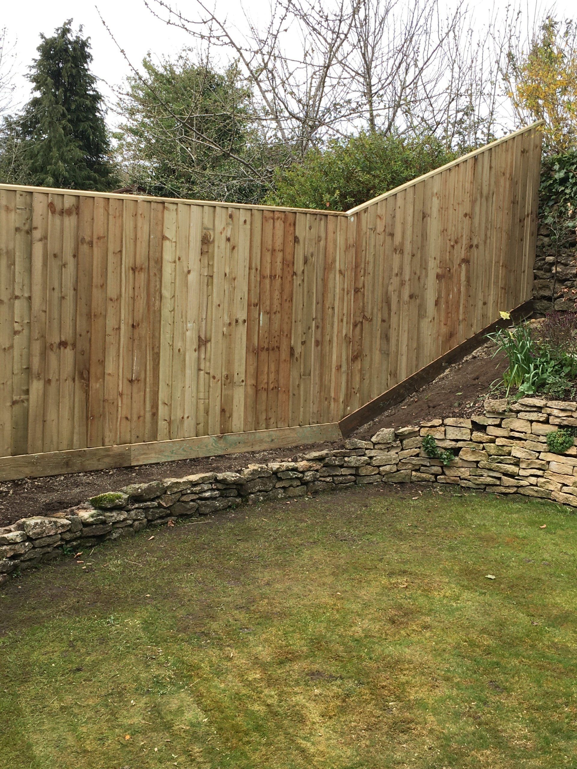 A wooden fence is surrounding a stone wall in a backyard.