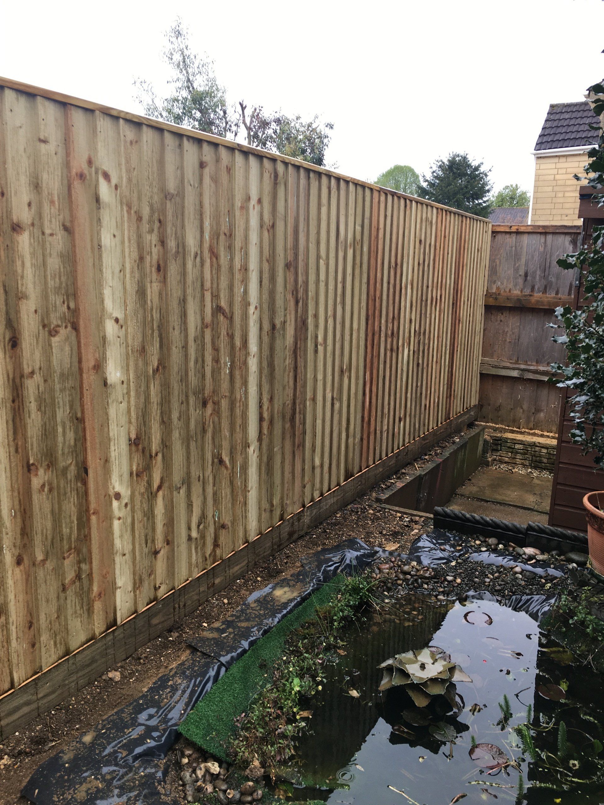 A wooden fence surrounds a pond in a backyard.