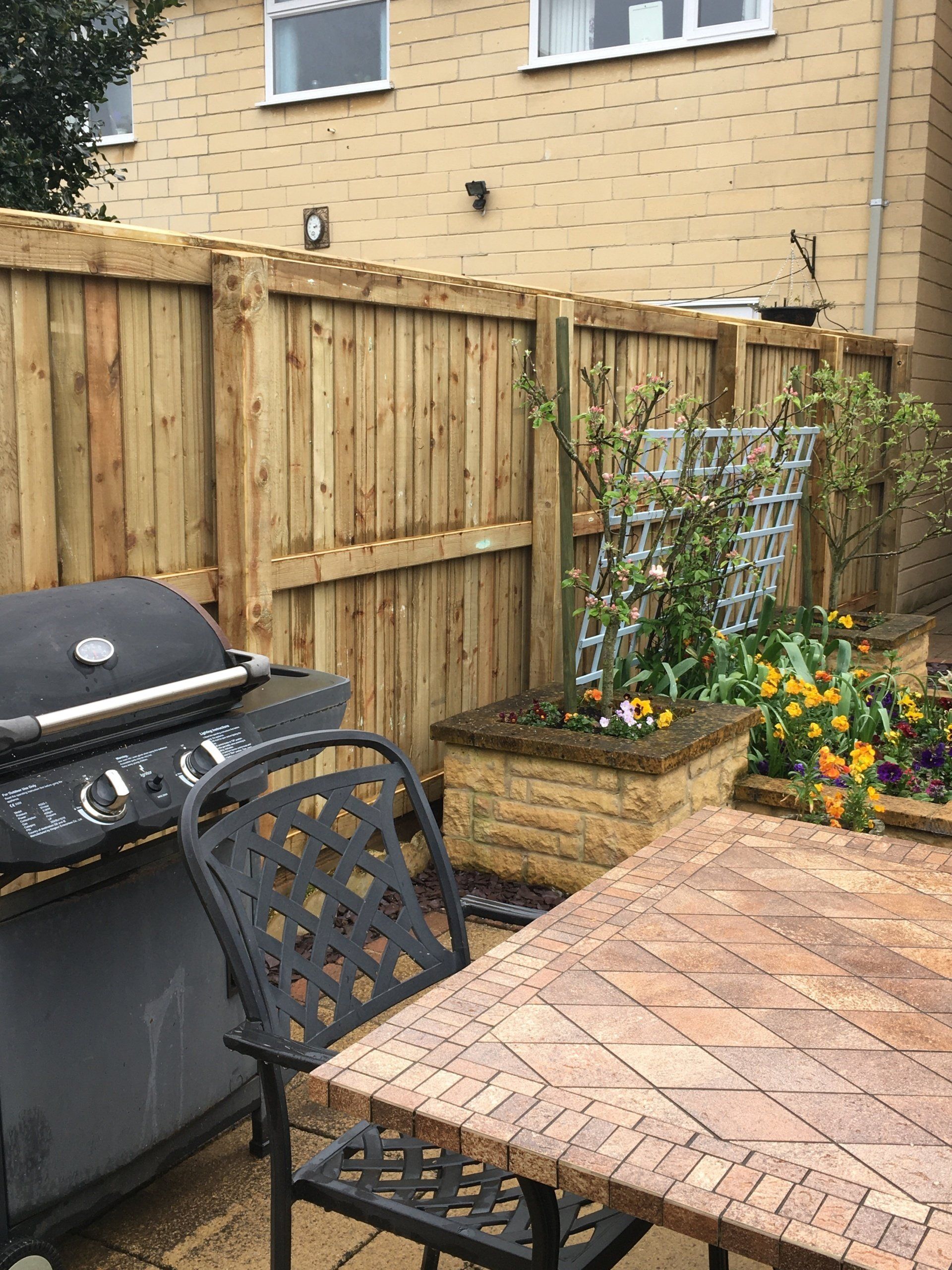 A wooden fence surrounds a patio area with a table and chairs.