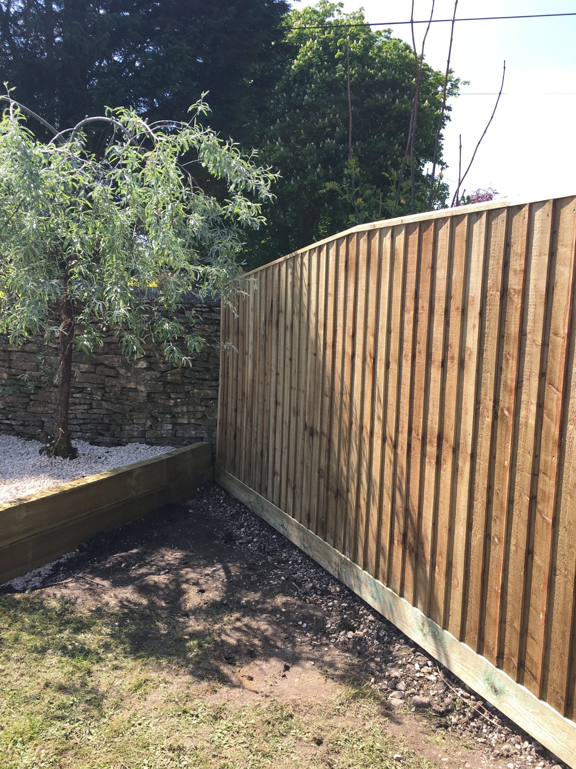 A wooden fence is surrounded by grass and trees in a backyard.
