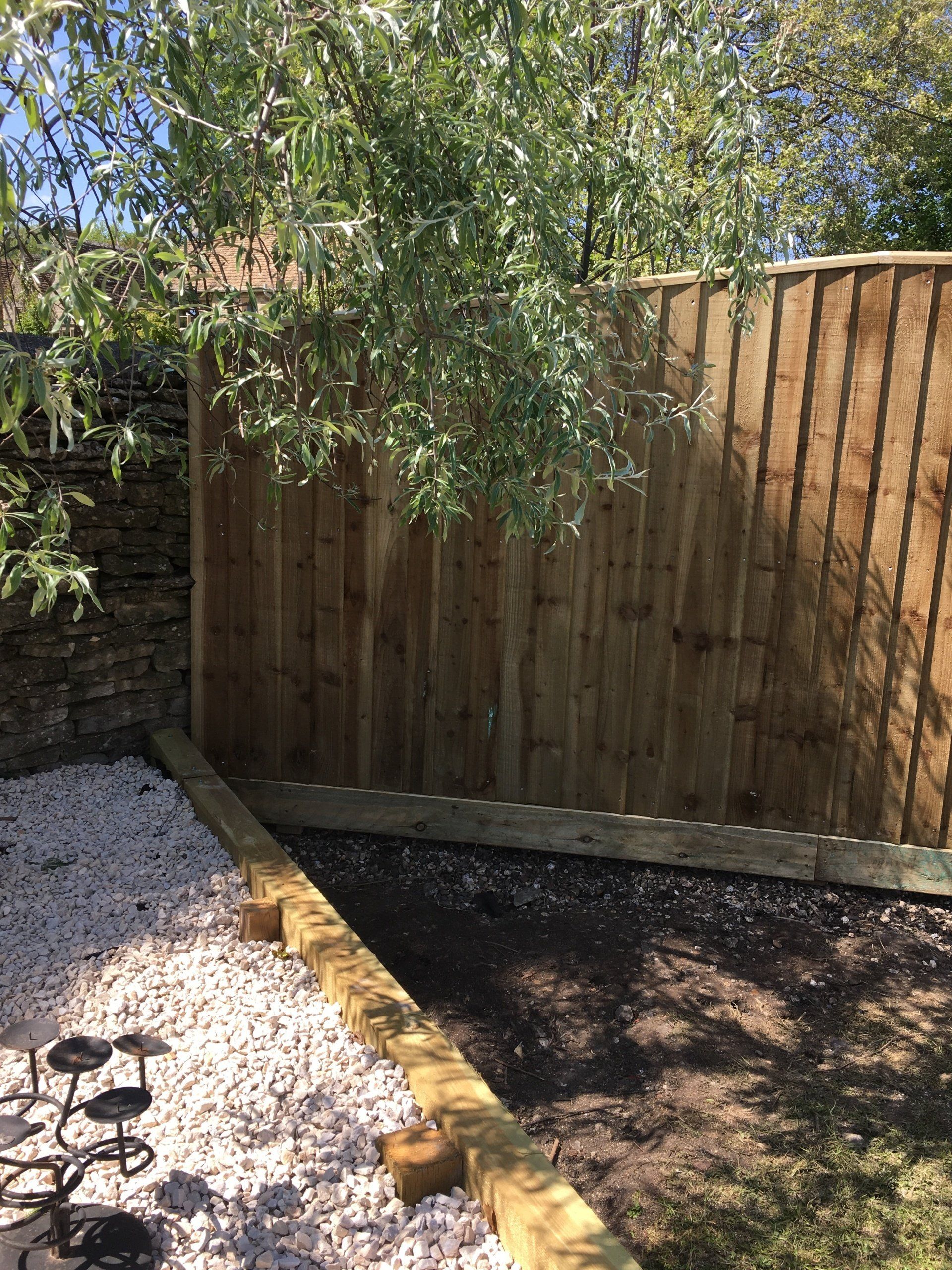 A wooden fence surrounds a gravel area in a backyard.