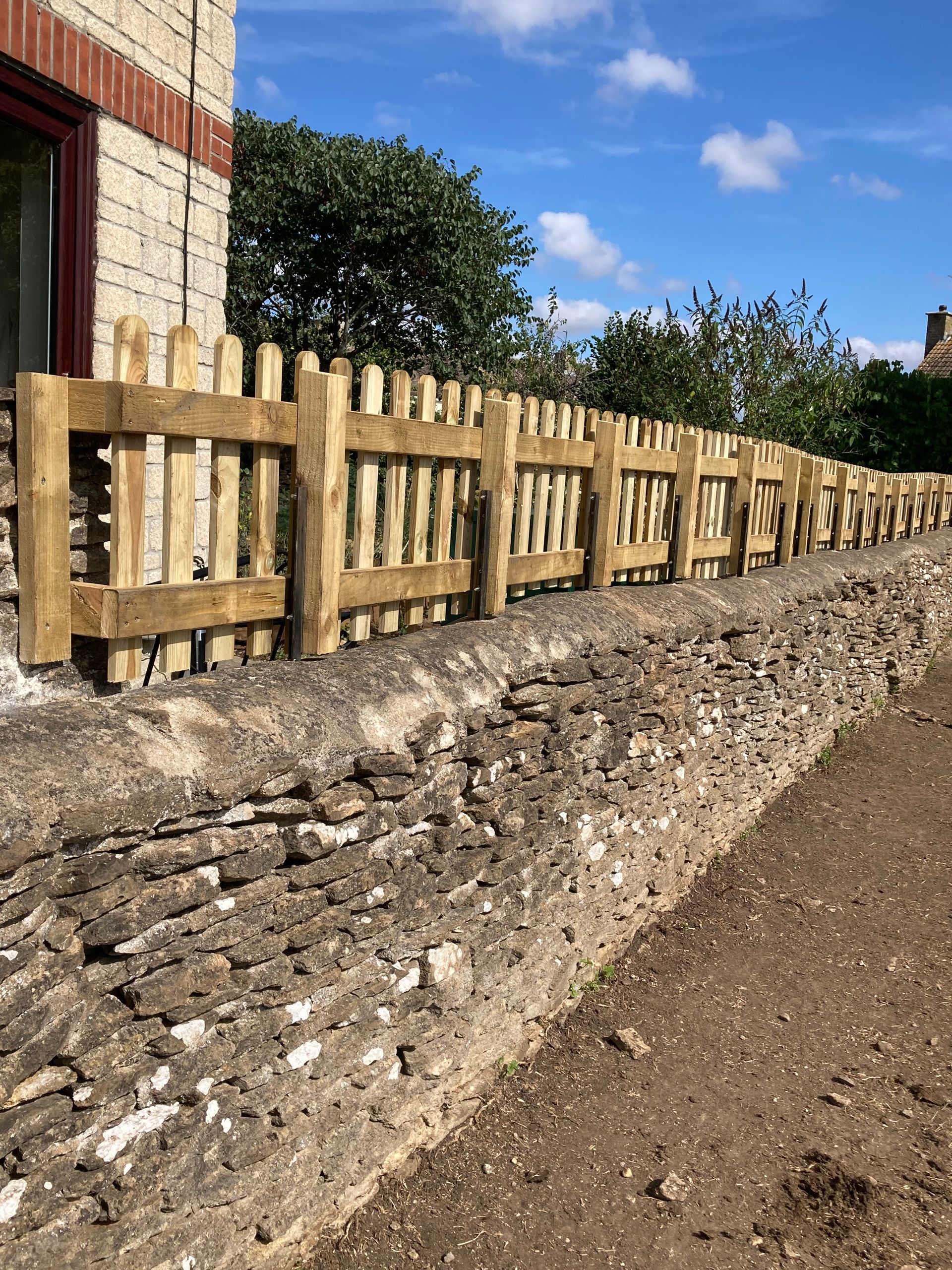 A wooden fence is sitting next to a stone wall.