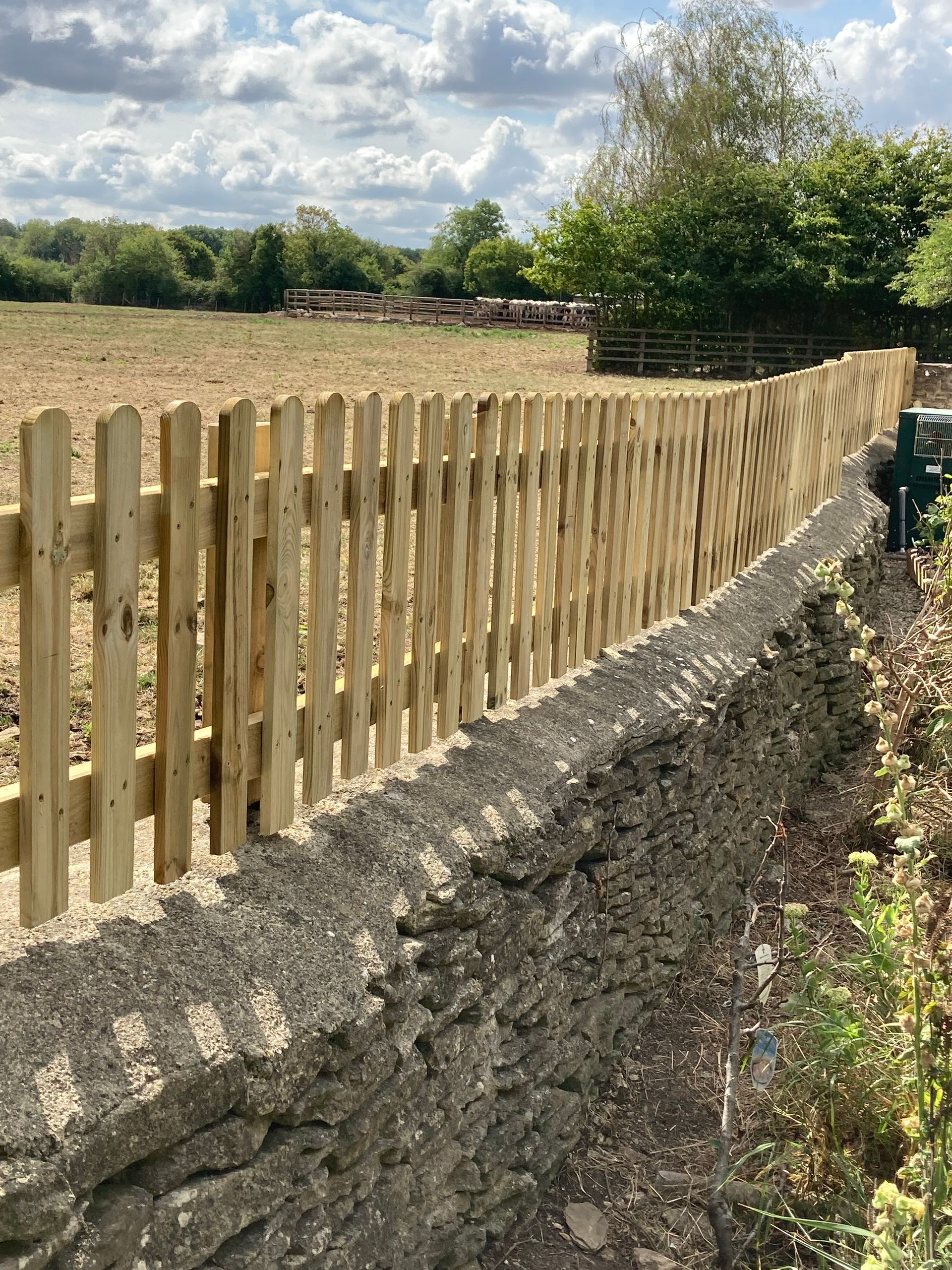 A wooden fence surrounds a stone wall in a field.