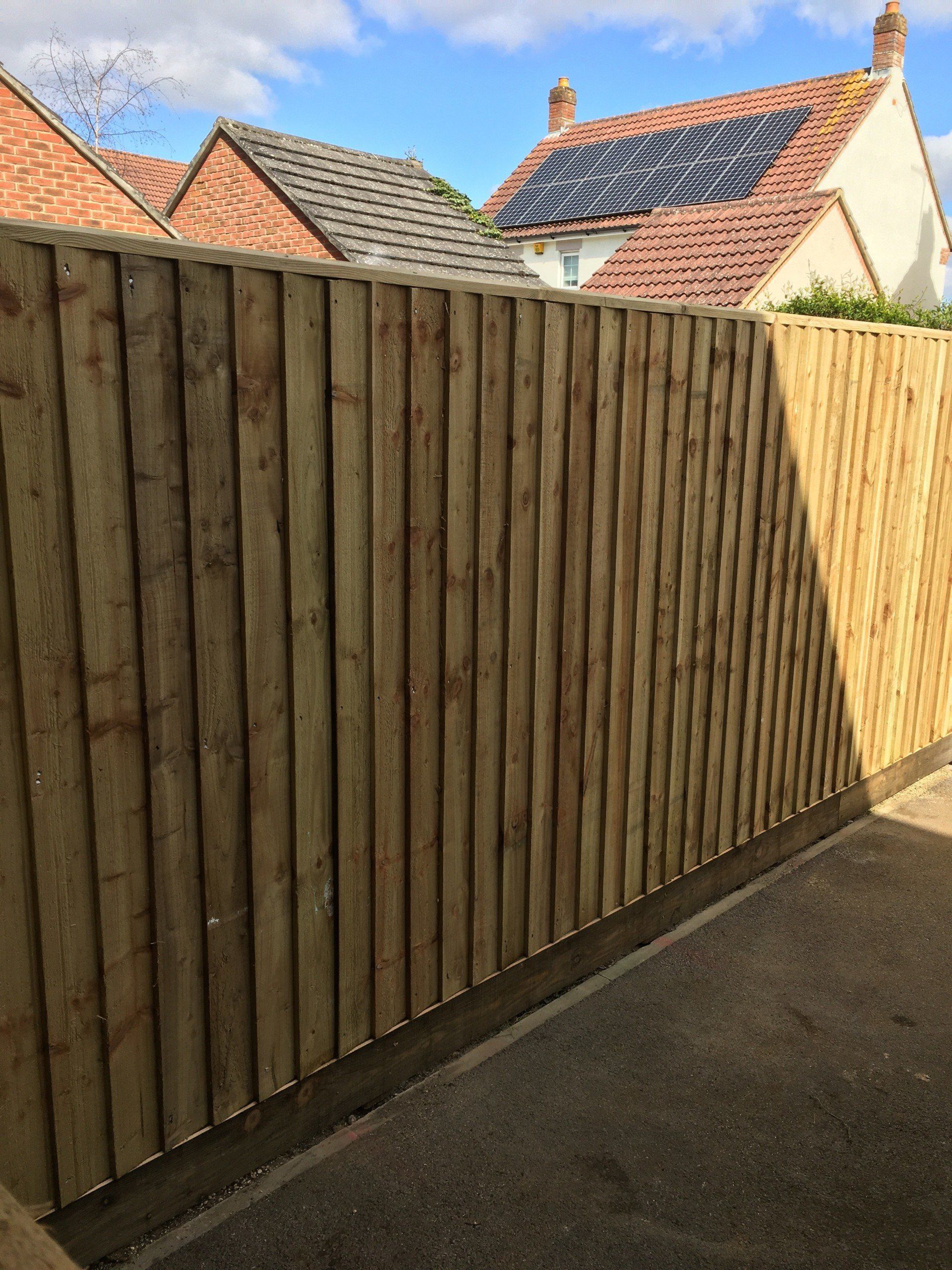 A wooden fence is in front of a house with solar panels on the roof.