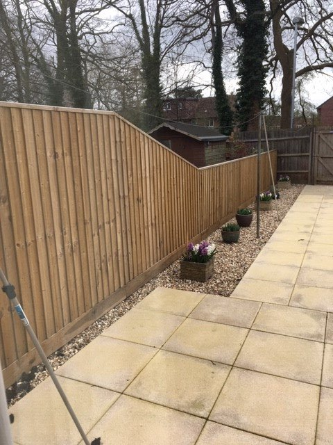 A wooden fence surrounds a patio with flowers in pots.