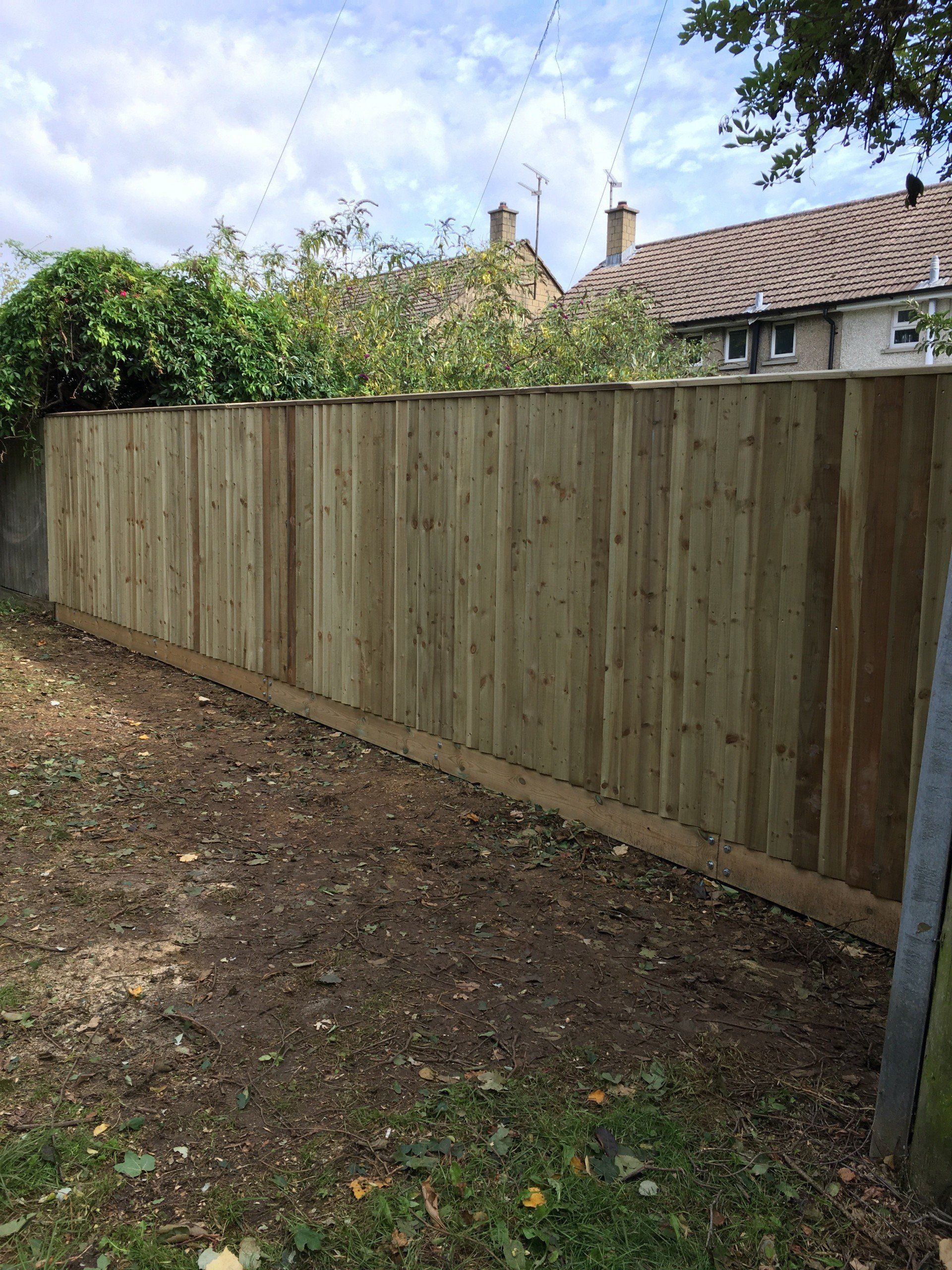 A wooden fence in a backyard with a house in the background.
