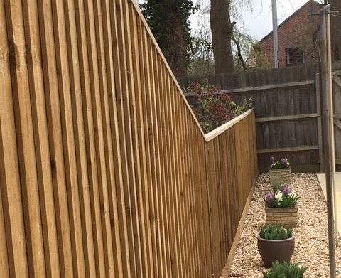 A wooden fence surrounds a gravel area with potted plants.