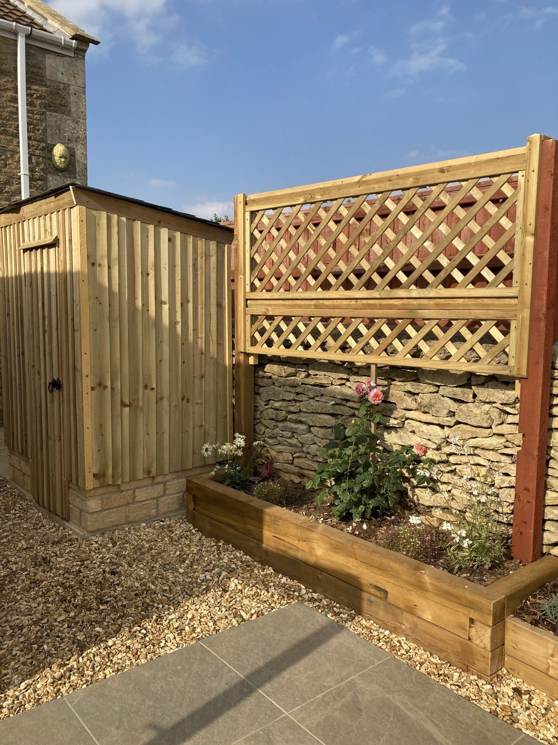 A wooden fence surrounds a stone wall in a garden.
