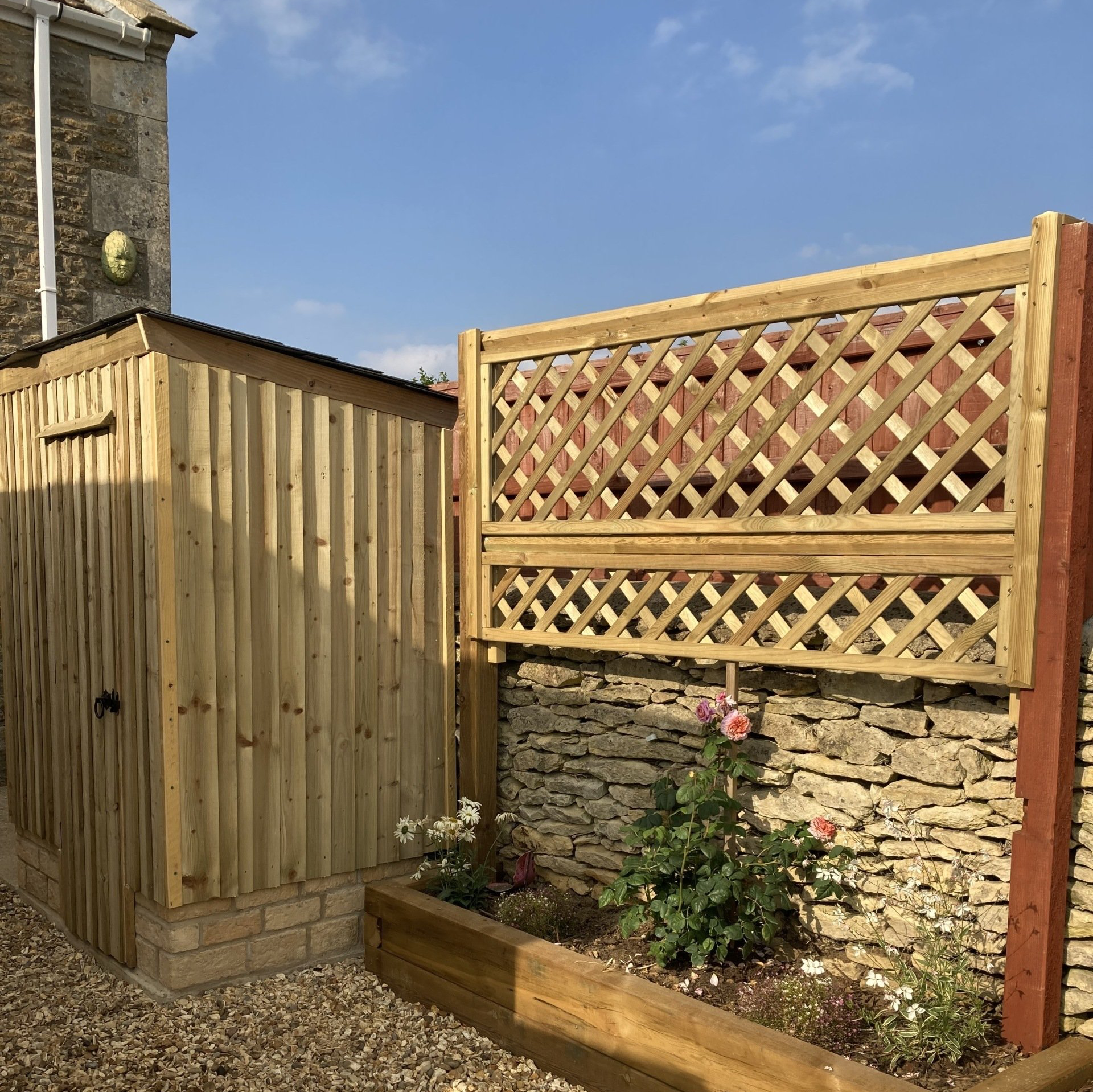 A wooden fence with a lattice on it is next to a stone wall.