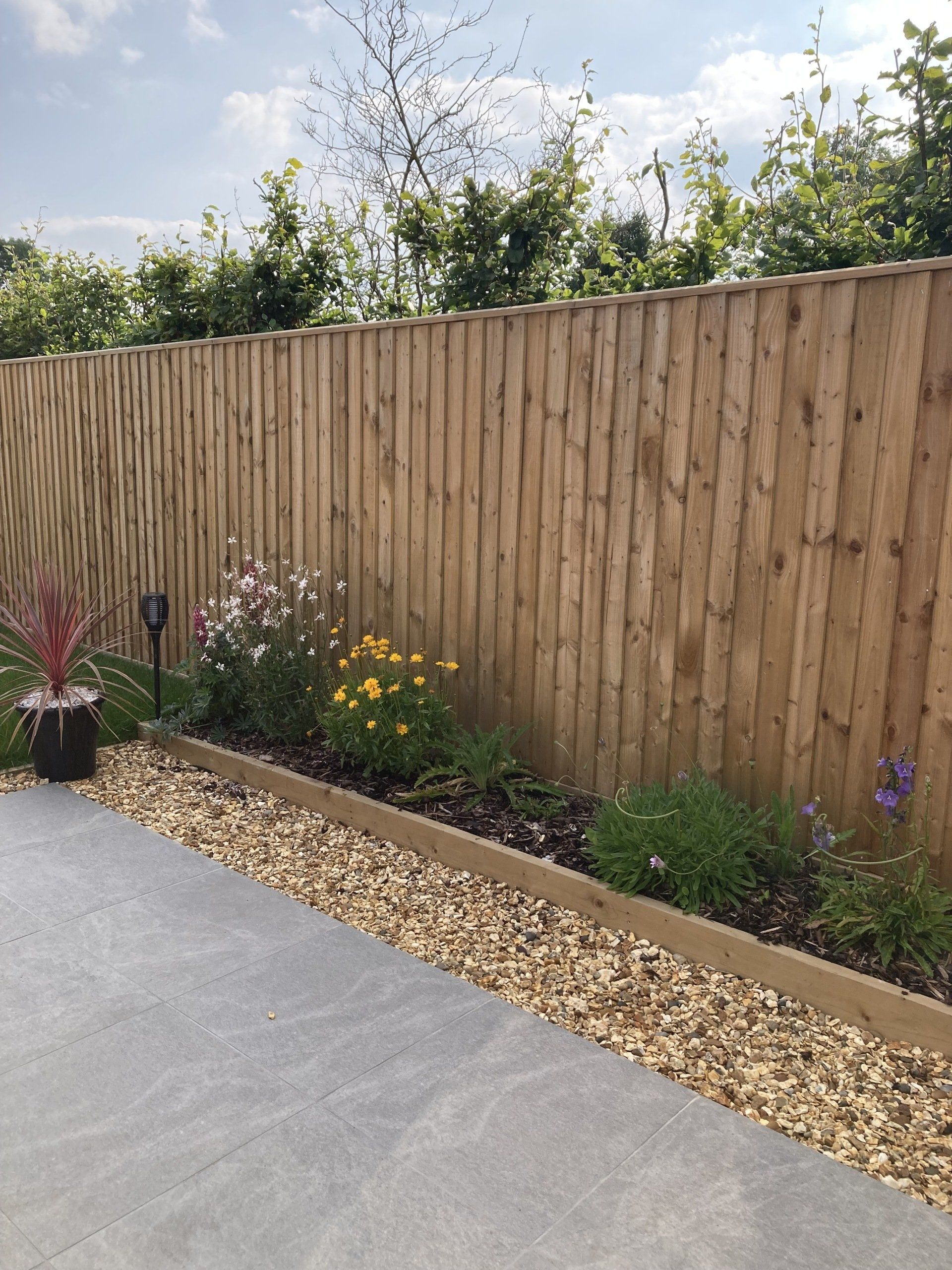 A wooden fence is surrounded by flowers and gravel.
