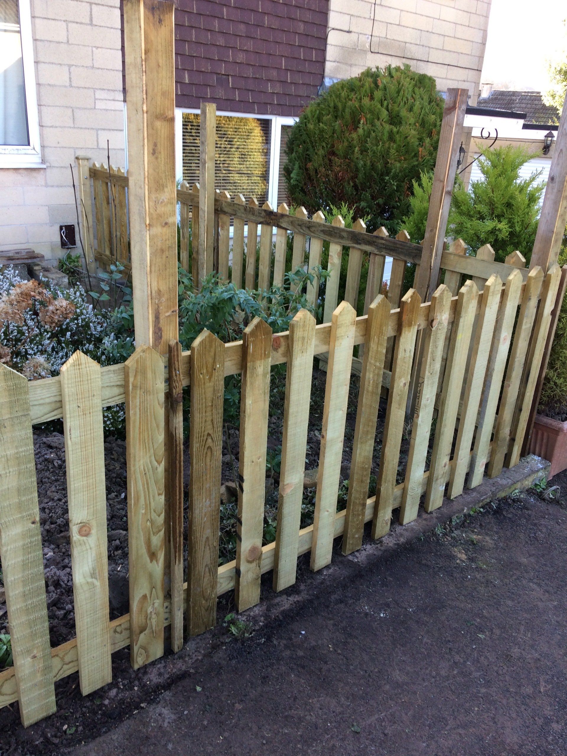 A wooden picket fence surrounds a garden in front of a house.