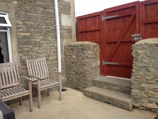 Two wooden chairs are sitting outside of a stone building next to a wooden gate
