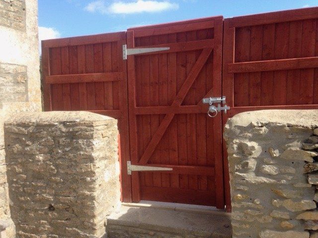 A red wooden gate is between two stone pillars
