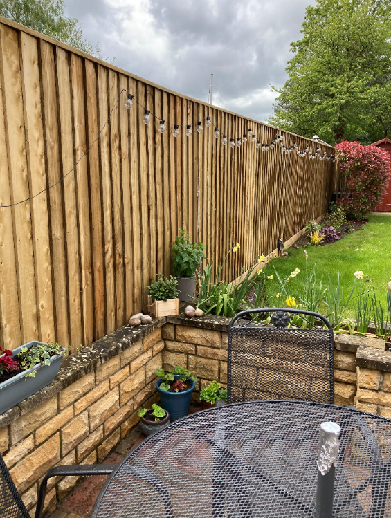 A wooden fence surrounds a patio area with a table and chairs.