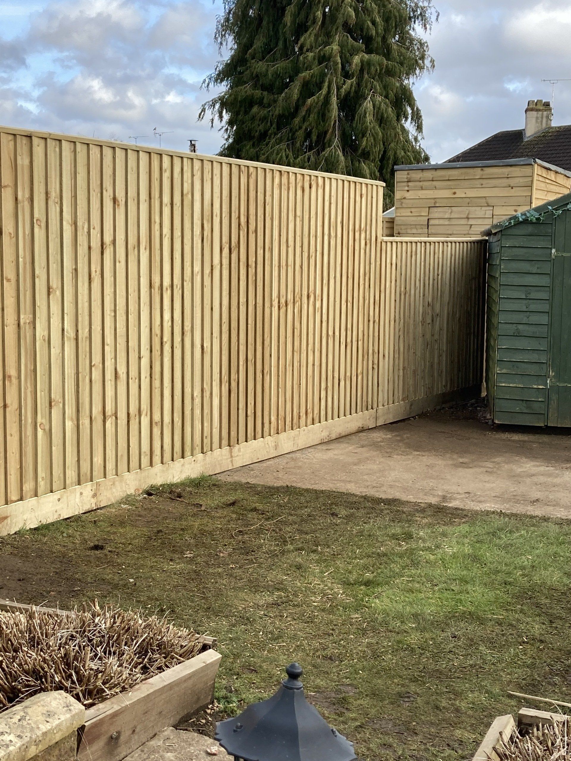 A wooden fence in a backyard next to a green shed.