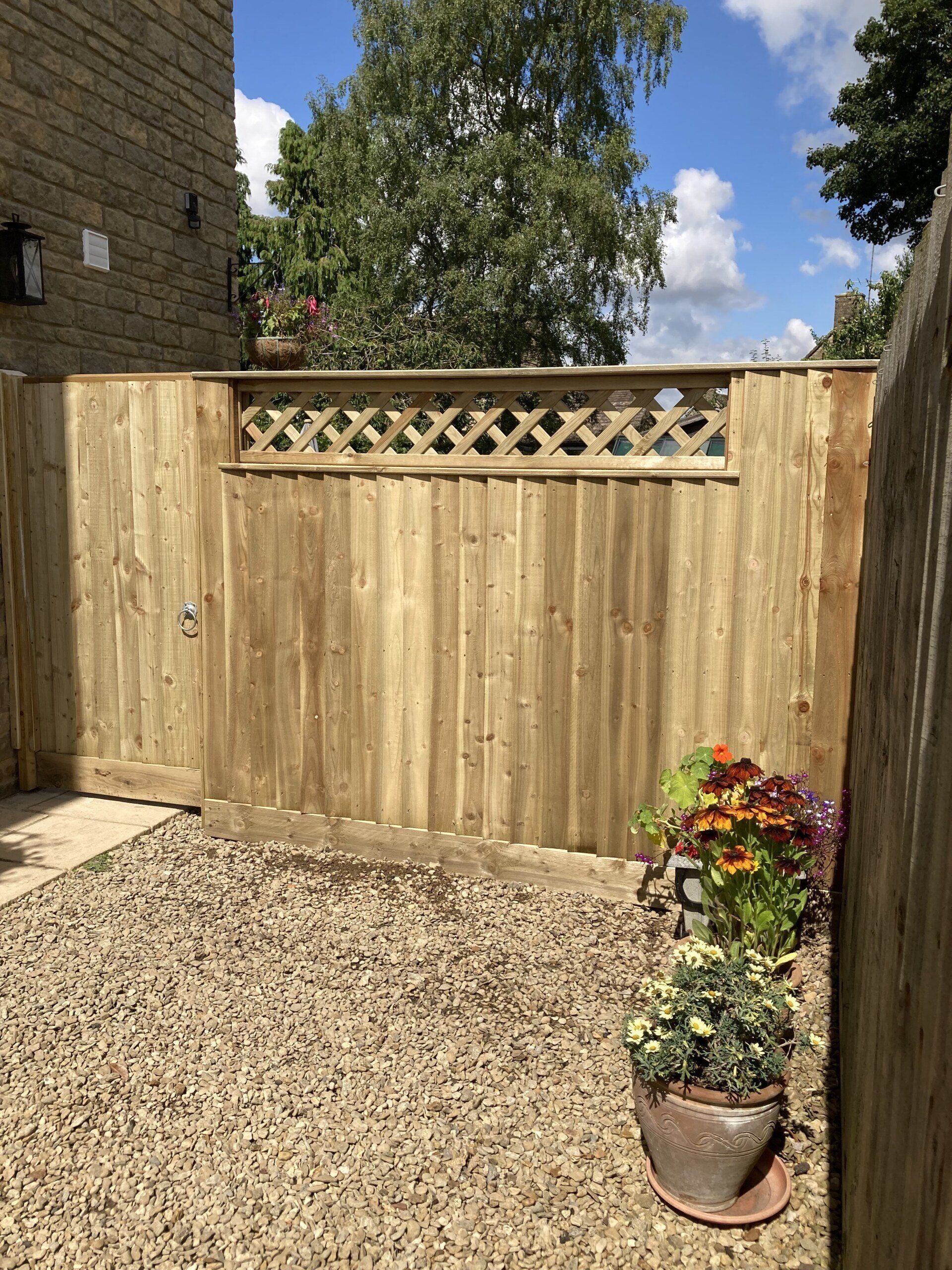 A wooden fence is surrounded by gravel and flowers in a garden.