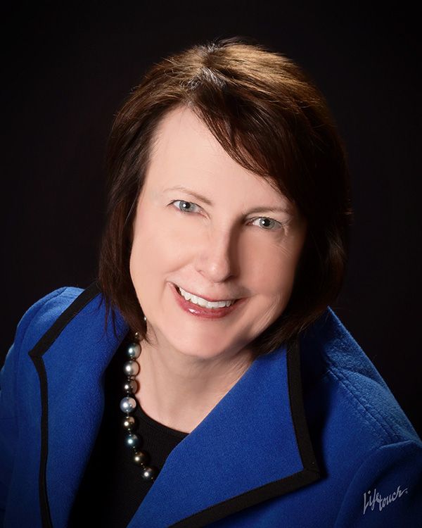 A woman wearing a blue jacket and pearls smiles for the camera