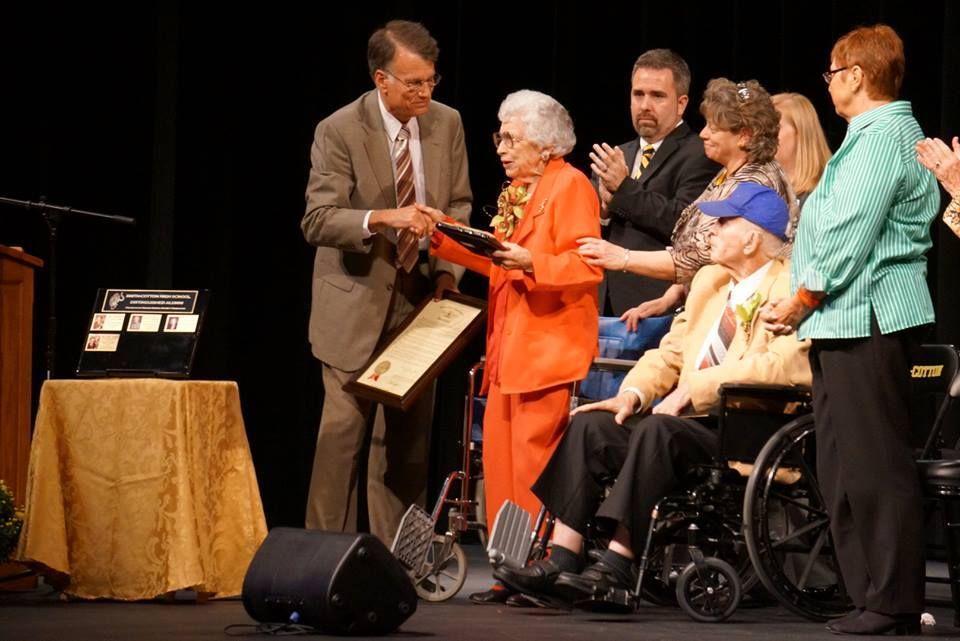 A man is giving an award to an elderly woman in a wheelchair