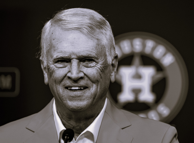 A man in a suit stands in front of a houston astros logo