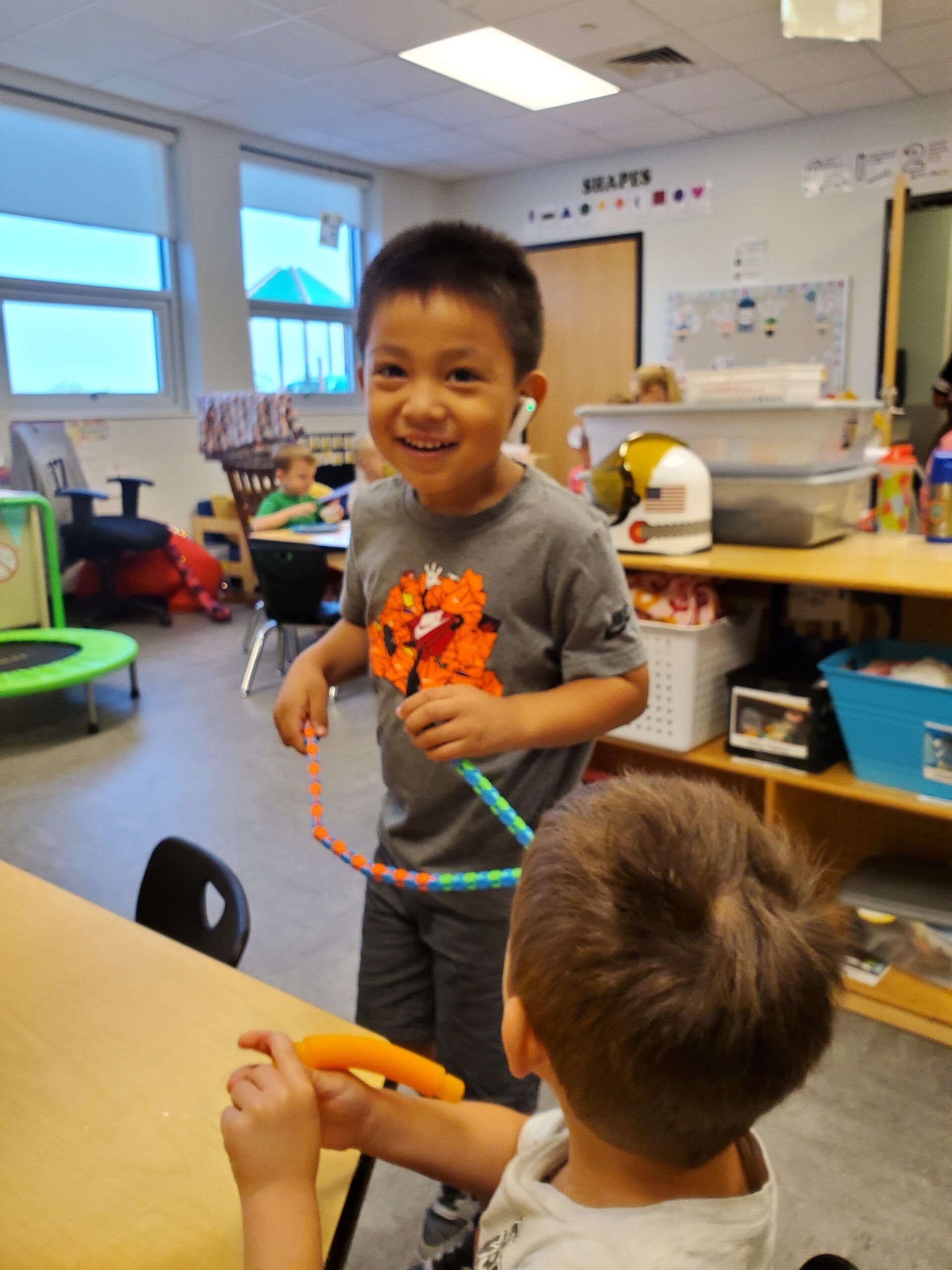 Two young boys are playing with a hula hoop in a classroom