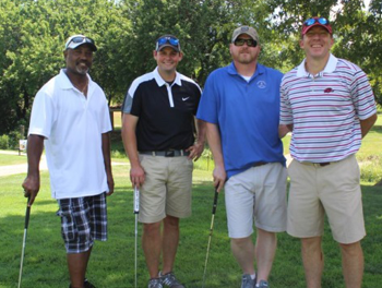 Four men standing on a golf course holding golf clubs