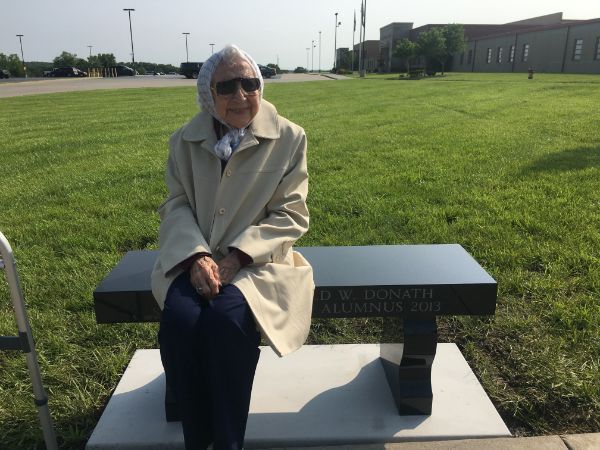 An elderly woman sits on a bench that says freedom park
