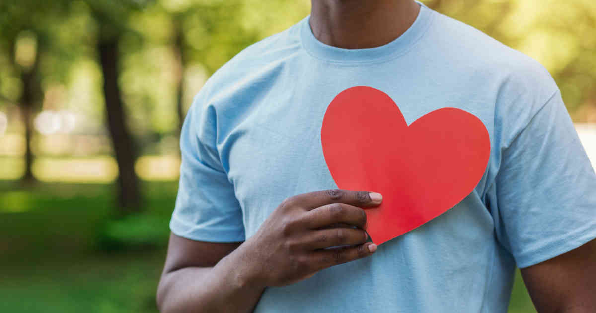 Un homme en chemise bleue tient un cœur rouge devant sa poitrine.