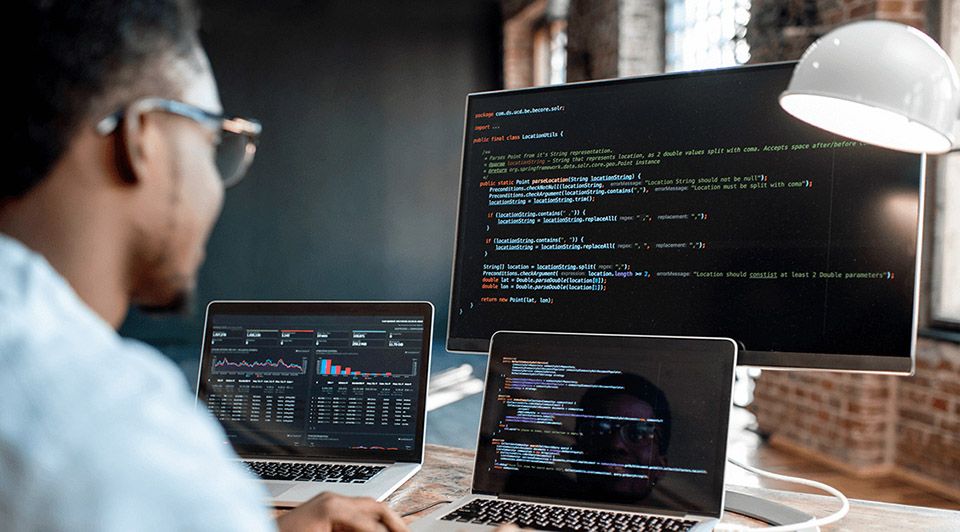 Un homme est assis à un bureau en utilisant un ordinateur portable et un ordinateur.