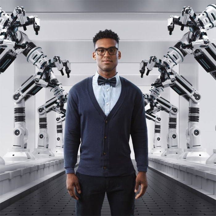 Un homme portant des lunettes et un nœud papillon se tient devant des bras robotisés