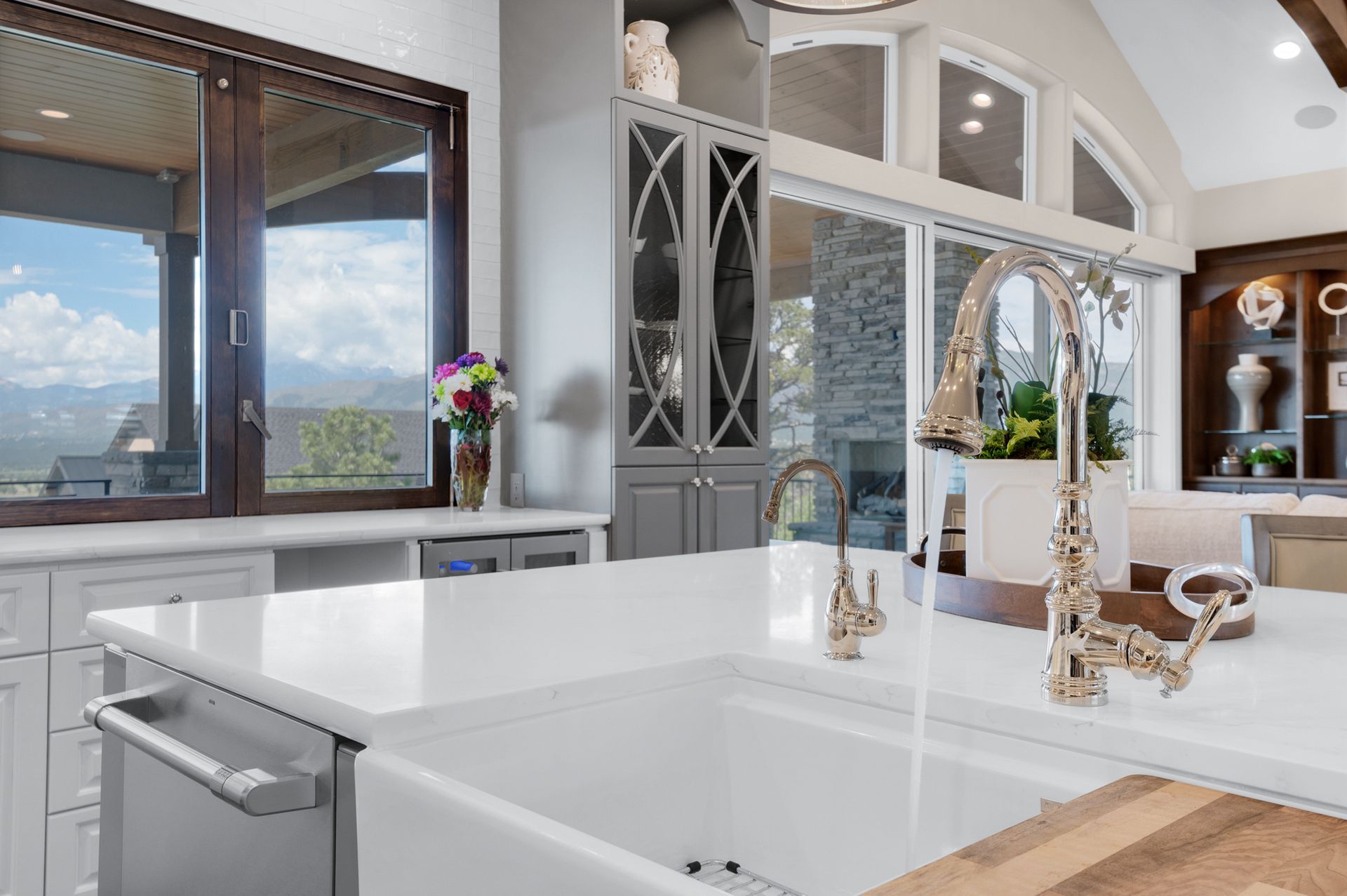 Kitchen with a white countertop and sink, stainless steel faucet, cabinets, and a mountain view through a large window.