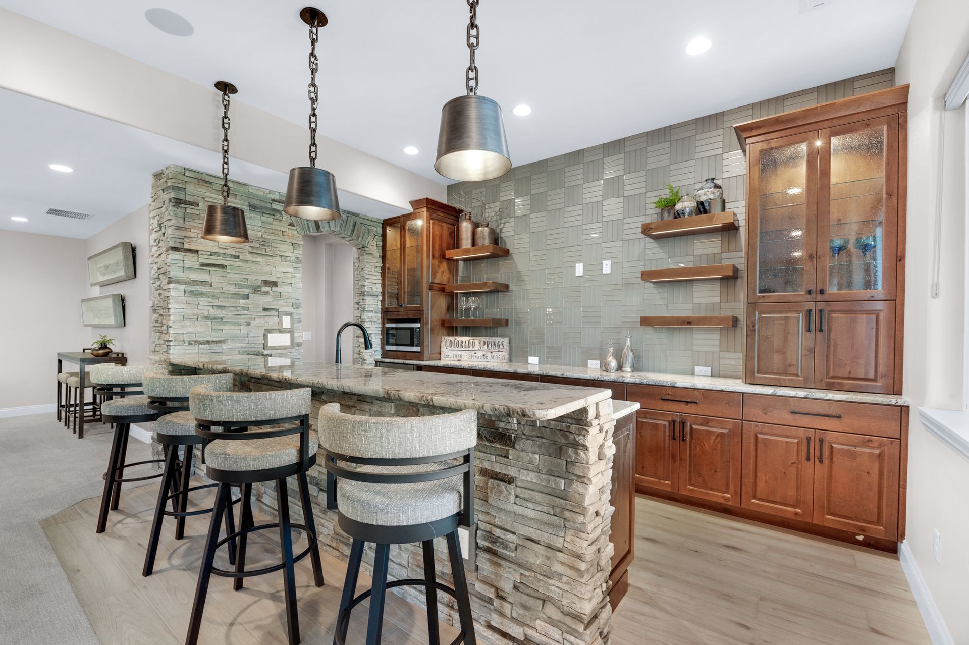 Basement bar with stone accents, wooden cabinetry, pendant lights, and bar stools.