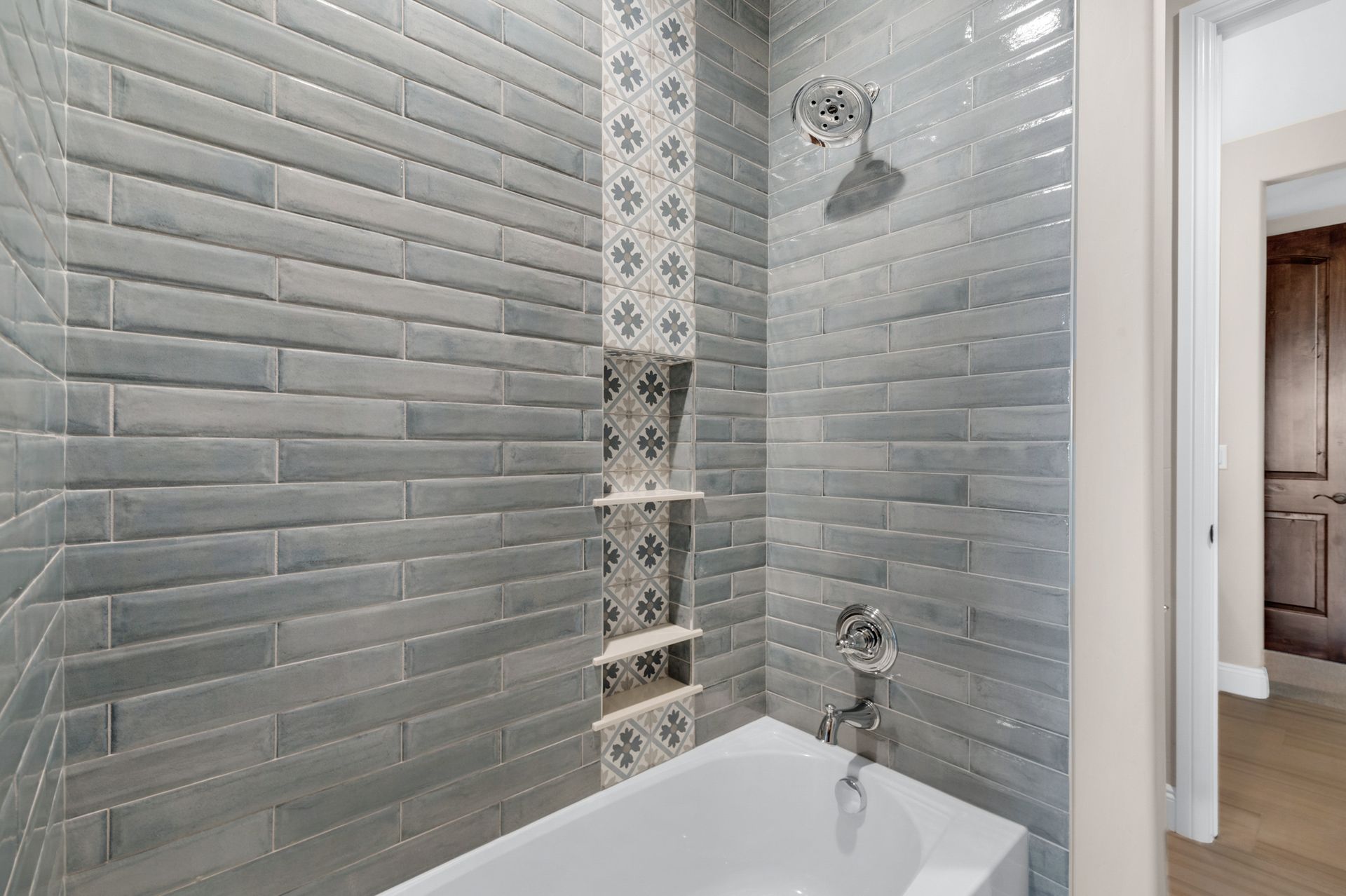Bathroom with gray brick tiles, a built-in shelf, and a showerhead over a white bathtub.