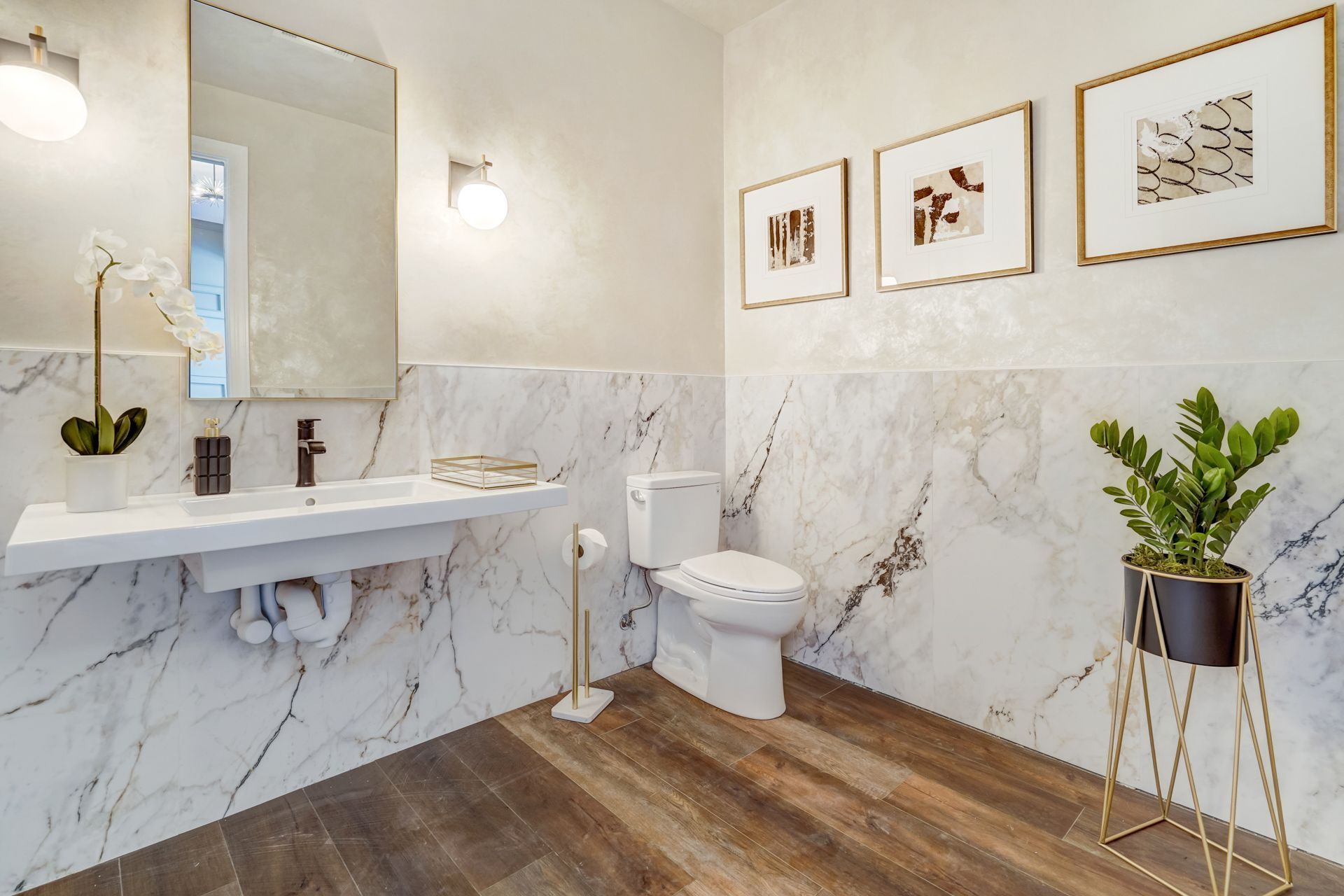 Modern bathroom with marble walls, floating sink, wood floor, and three framed art pieces.