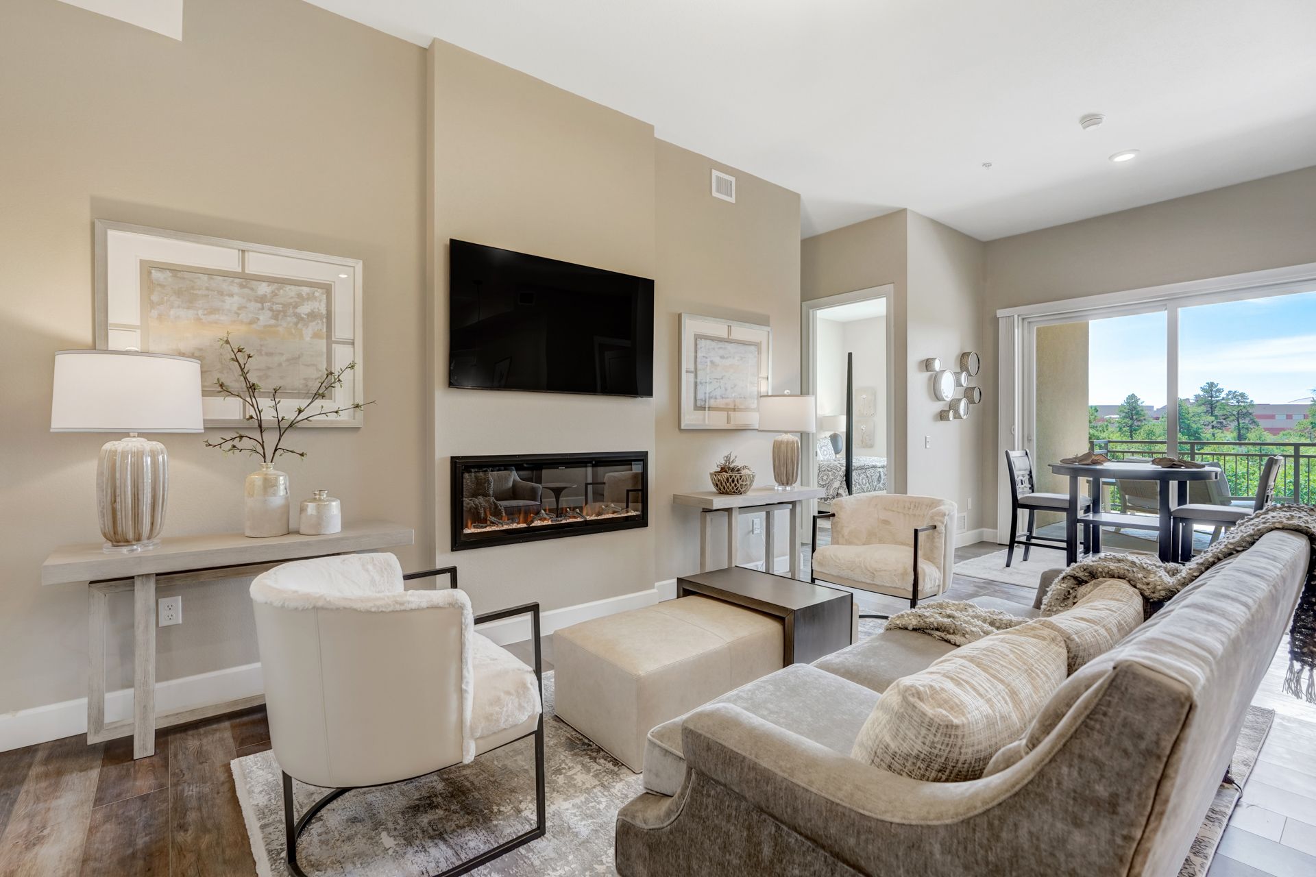 Elegant living room with beige walls, sofa, and TV over fireplace, with a sliding door to a balcony.