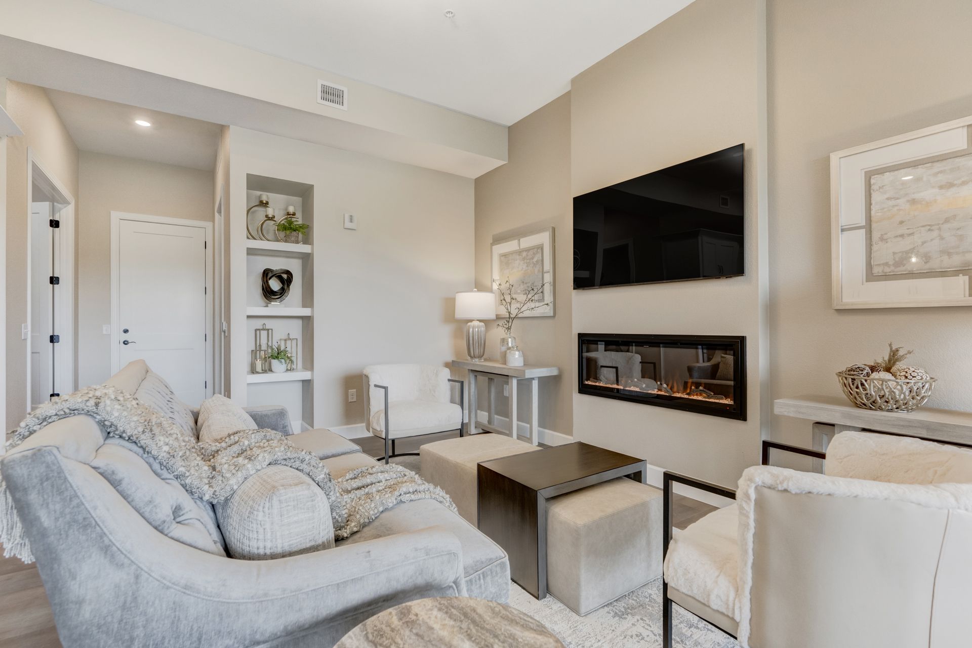 Cozy living room with a fireplace, TV, neutral-toned furniture, and decorative shelves.