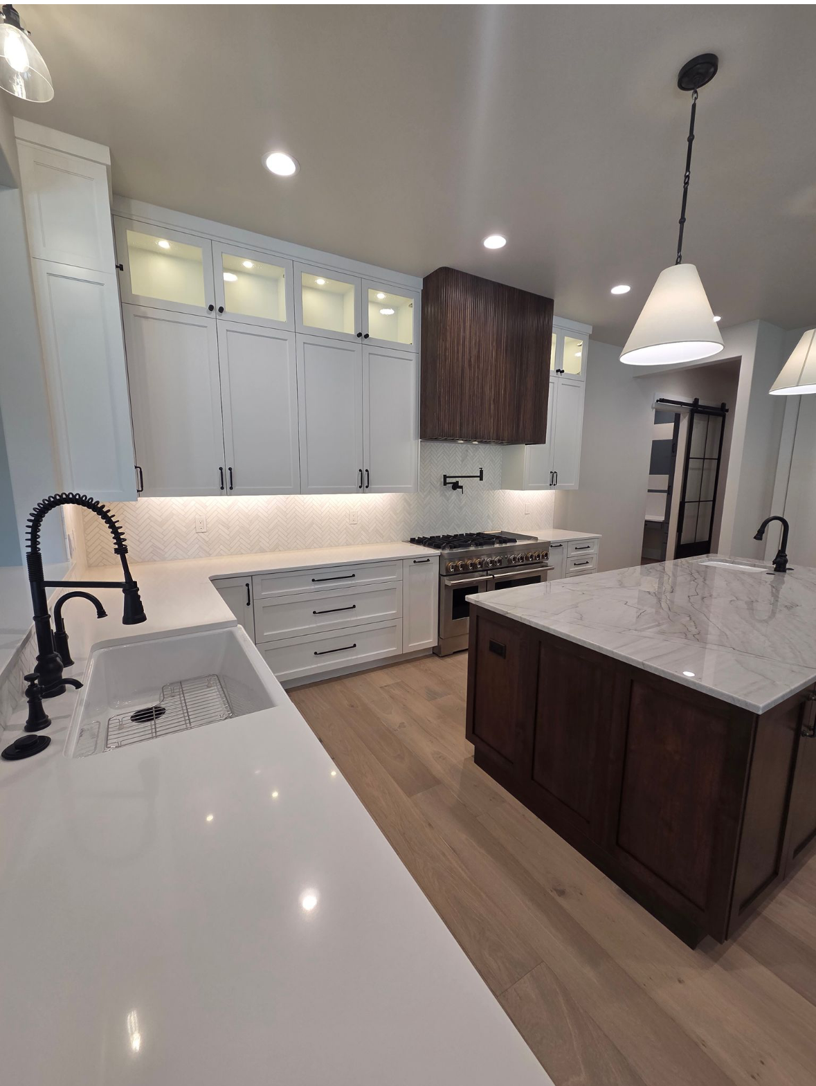 Modern kitchen with white cabinets, dark island, wood hood, and marble countertops.