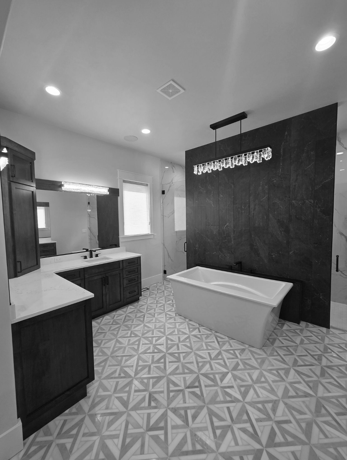 Modern bathroom with dark cabinets, patterned floor, freestanding tub, and decorative lighting.