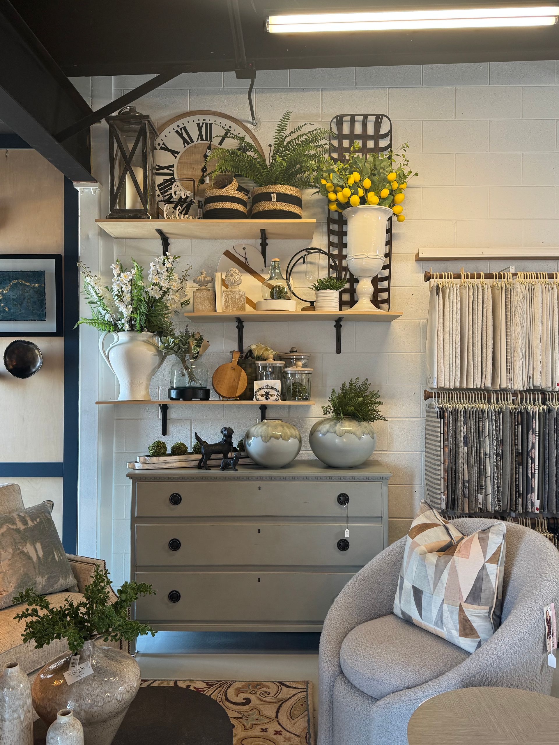 A decorated home interior display with shelves of decor, grey dresser, and cozy armchair.