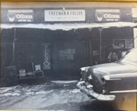 A black and white photo of a car parked in front of a building.