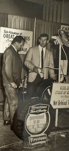 Two men are standing next to a motorcycle in a black and white photo.