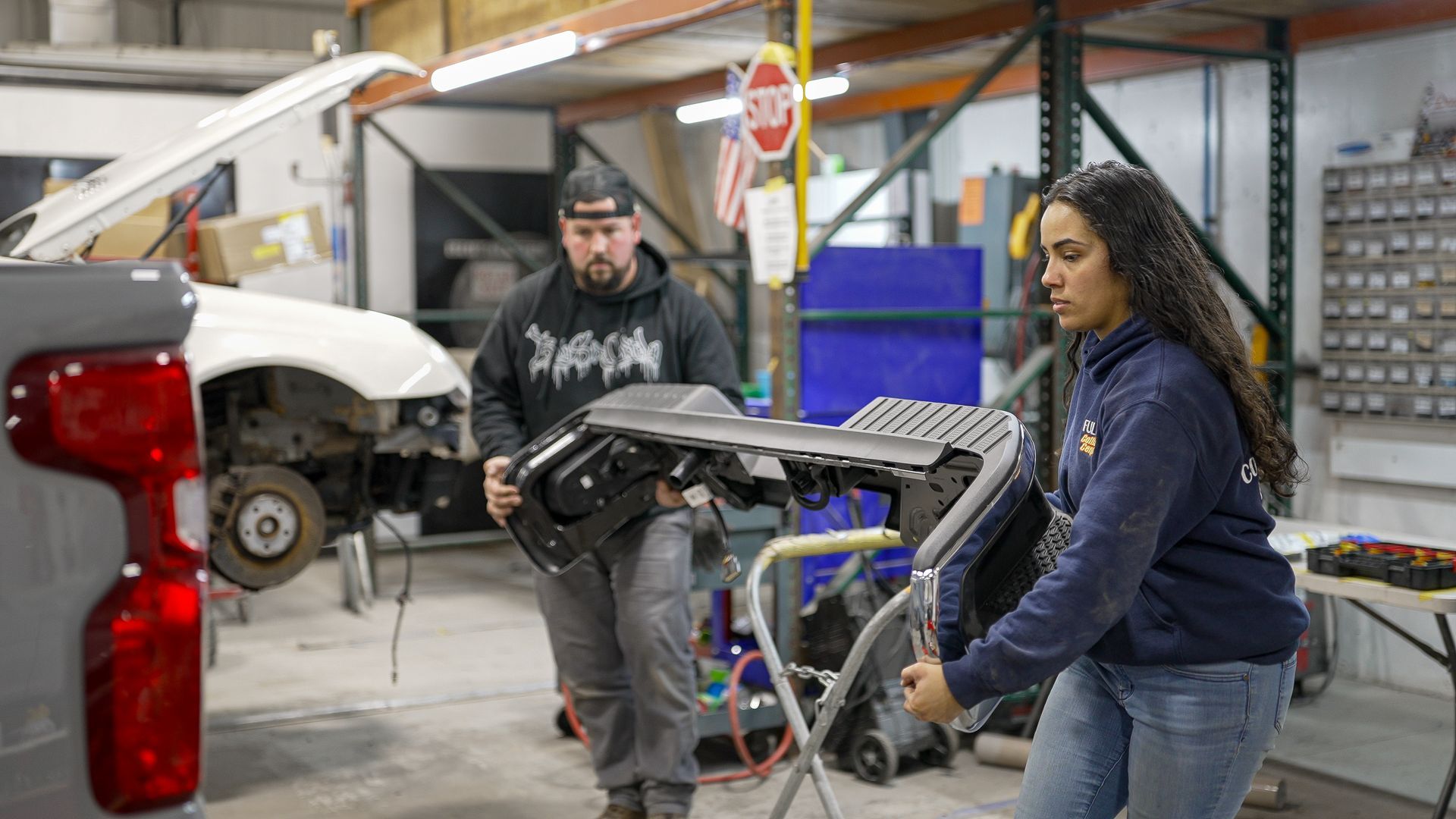 A man and a woman are working on a car in a garage.