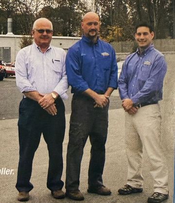 Three men in blue shirts are posing for a picture