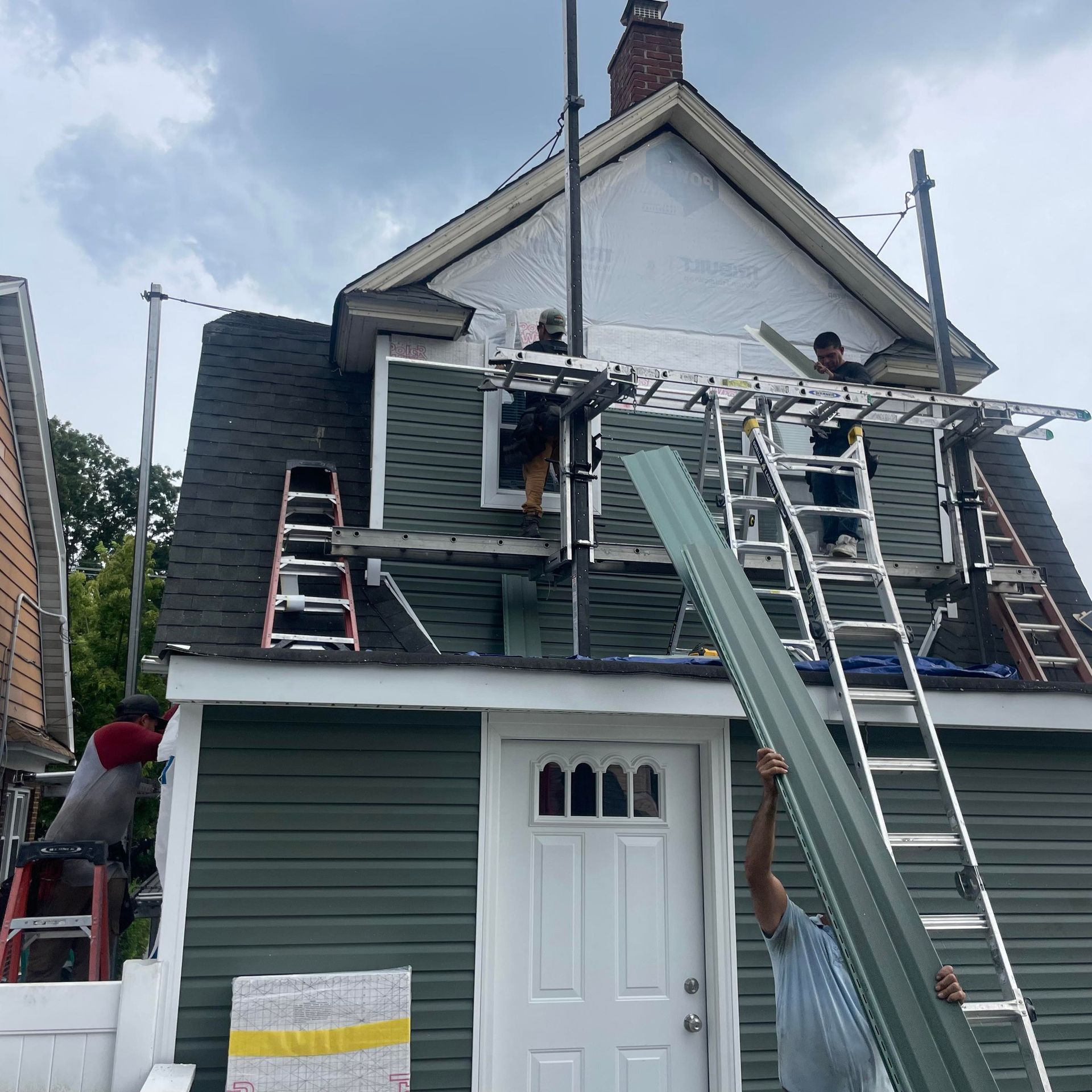 A man on a ladder is holding a piece of metal on the roof of a house.